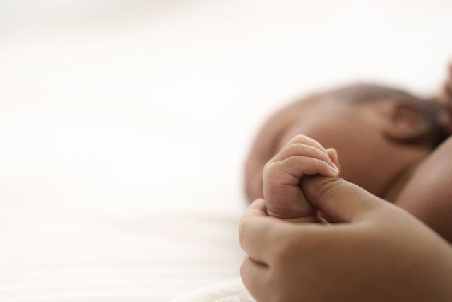 Mother holding hand of newborn while bonding during state disability time